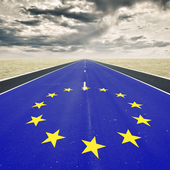 A very long road, with tarmac painted like the EU flag, stretches into the distance