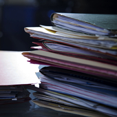 Piles of paper folders containing documents on top of a desk