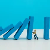 A model of a man holding up a row of collapsing dominos