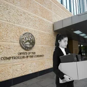 A woman stands outside the OCC building holding a cardboard box, because she has lost her job. Image is created, not real-life.