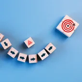 Curved line of blocks with direction arrows, with danger symbols to the side of the line, which leads to a bull’s-eye target block with an arrow in it