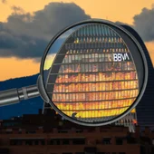 Magnifying glass highlights BBVA’s Madrid building with a cloudy, sunset background